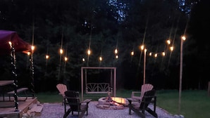 Ein Außenbereich mit zwei Adirondack-Stühlen, einer Feuerstelle und Lichterketten.