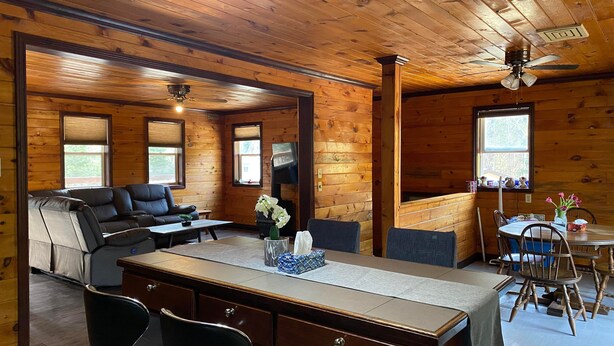 Ein gemütliches Blockhaus-Interieur mit Holzausbau, einer Couch, einem Esstisch und einem Kamin.
