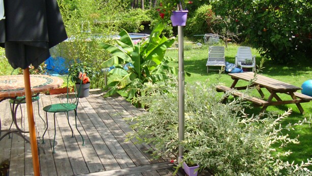 Eine Holzterrasse mit Gartenmöbeln, einem Picknicktisch und Kübelpflanzen.