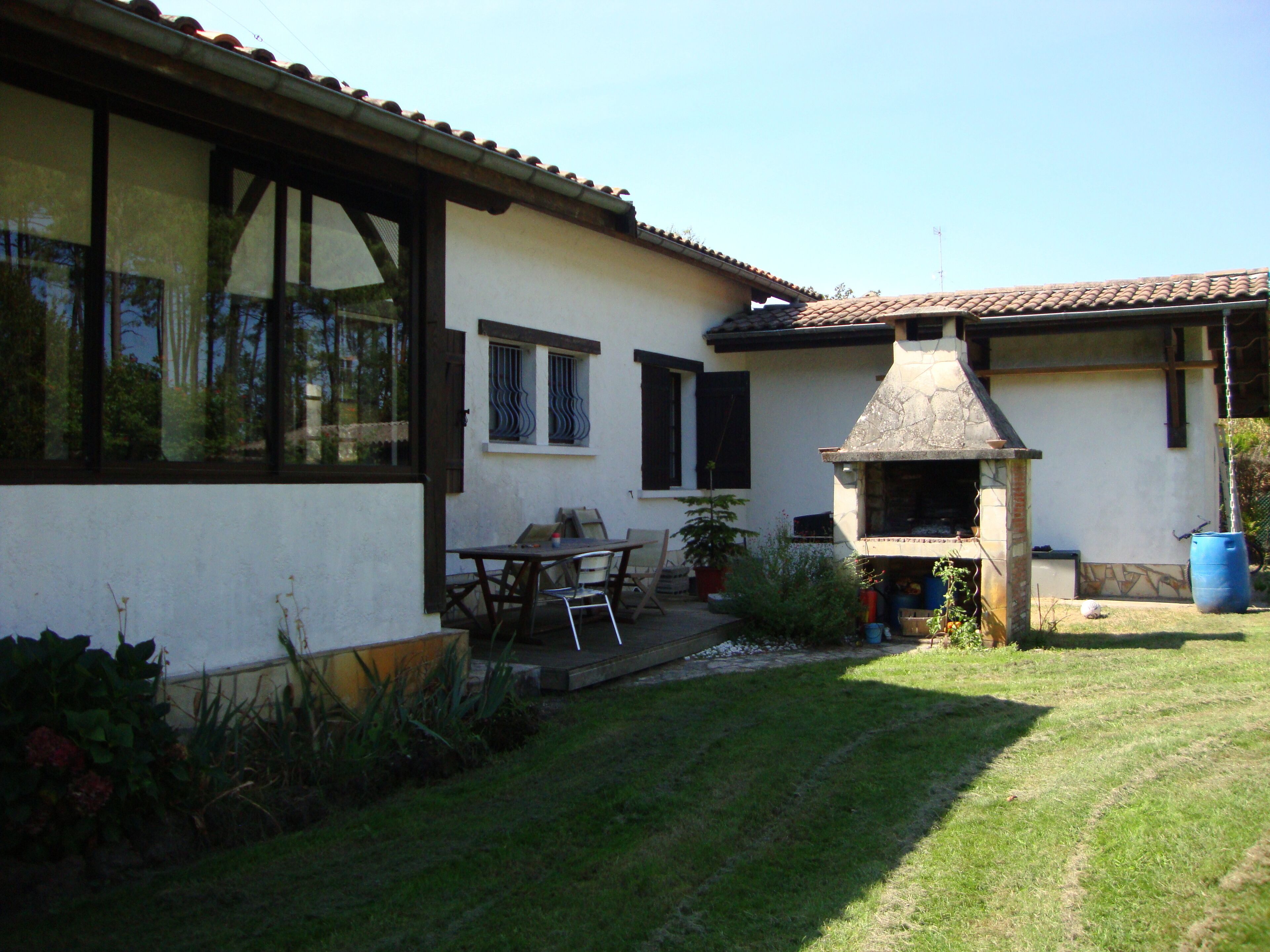 Een huis met een terras, een barbecuehoek en een kleine tuin.