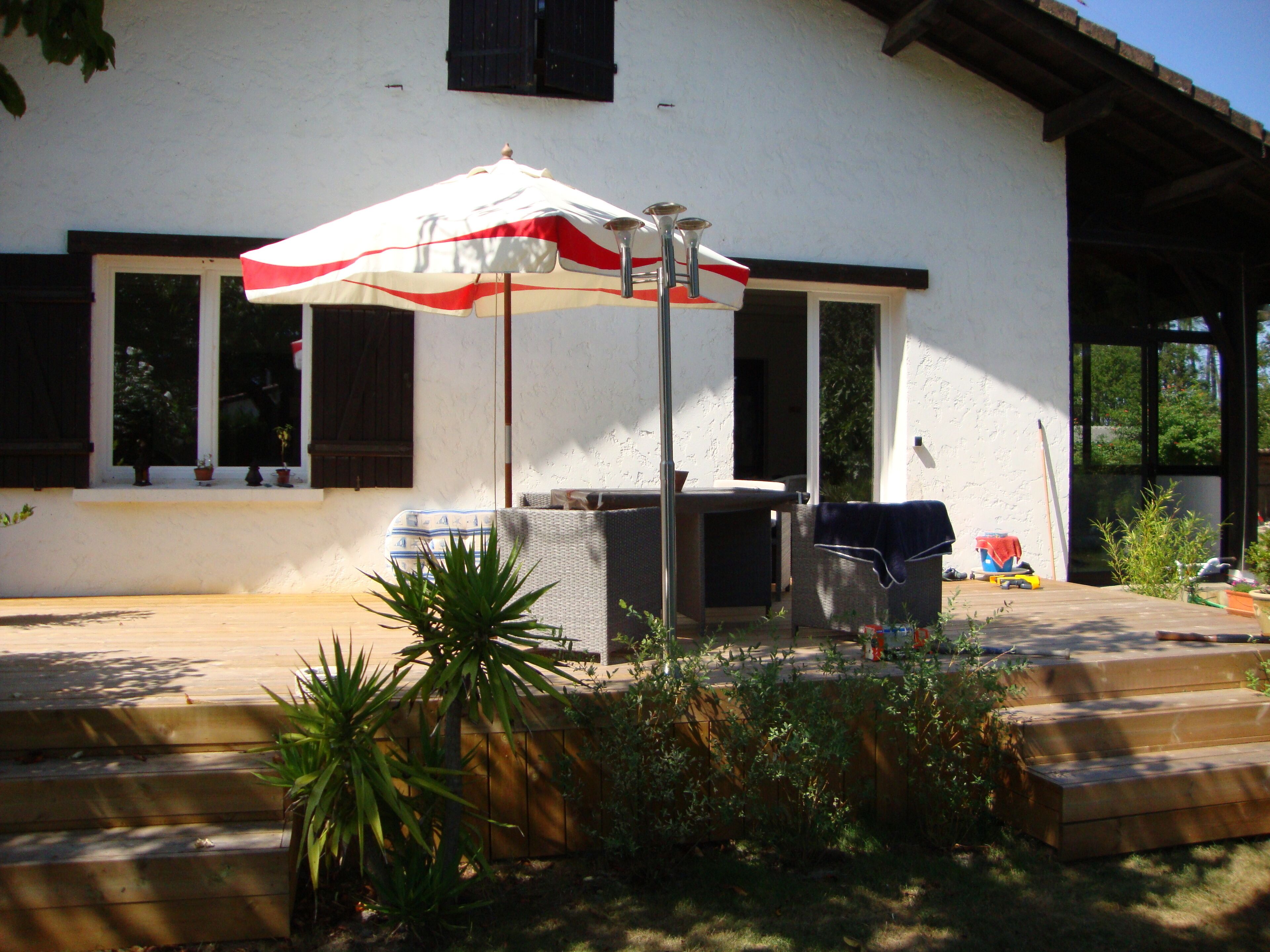 Un patio con mesa y sillas, un espacio cubierto con sombrilla y un pequeño jardín con plantas.