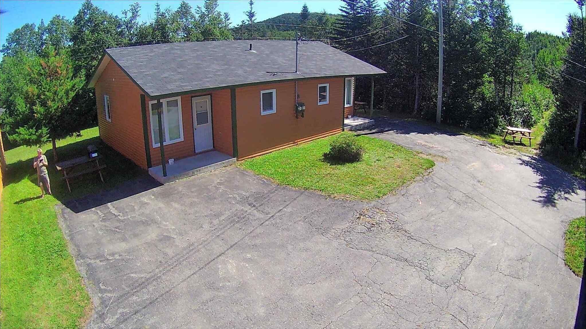 A single-story brick house with a sloped roof, a front porch, and a small front yard with a lawn and a bush.