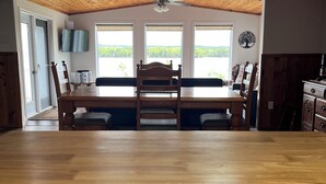 Een eethoek met een houten tafel en stoelen, een plafondventilator en uitzicht door grote ramen.