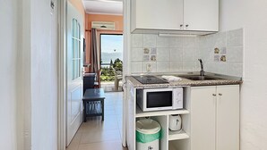 A compact kitchen with white cabinets, a microwave, and a sink. There's a small trash bin and a window with a view of greenery. - Sea view Apartment P/4 (Benitses, Corfu)