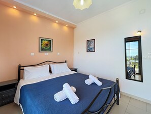 A bedroom with a bed, two paintings, a window with a view, and a ceiling light.