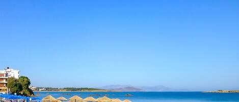 Relax on the beach with comfortable lounge chairs and umbrellas, overlooking the ocean and distant mountains.