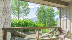 Ein Balkon mit Glasgeländer, einem Korbstuhl und Blick auf Bäume und Berge.