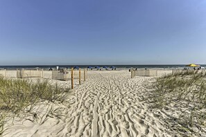 Een zandpad langs het strand dat naar de oceaan leidt, met strandparasols en een houten hek.