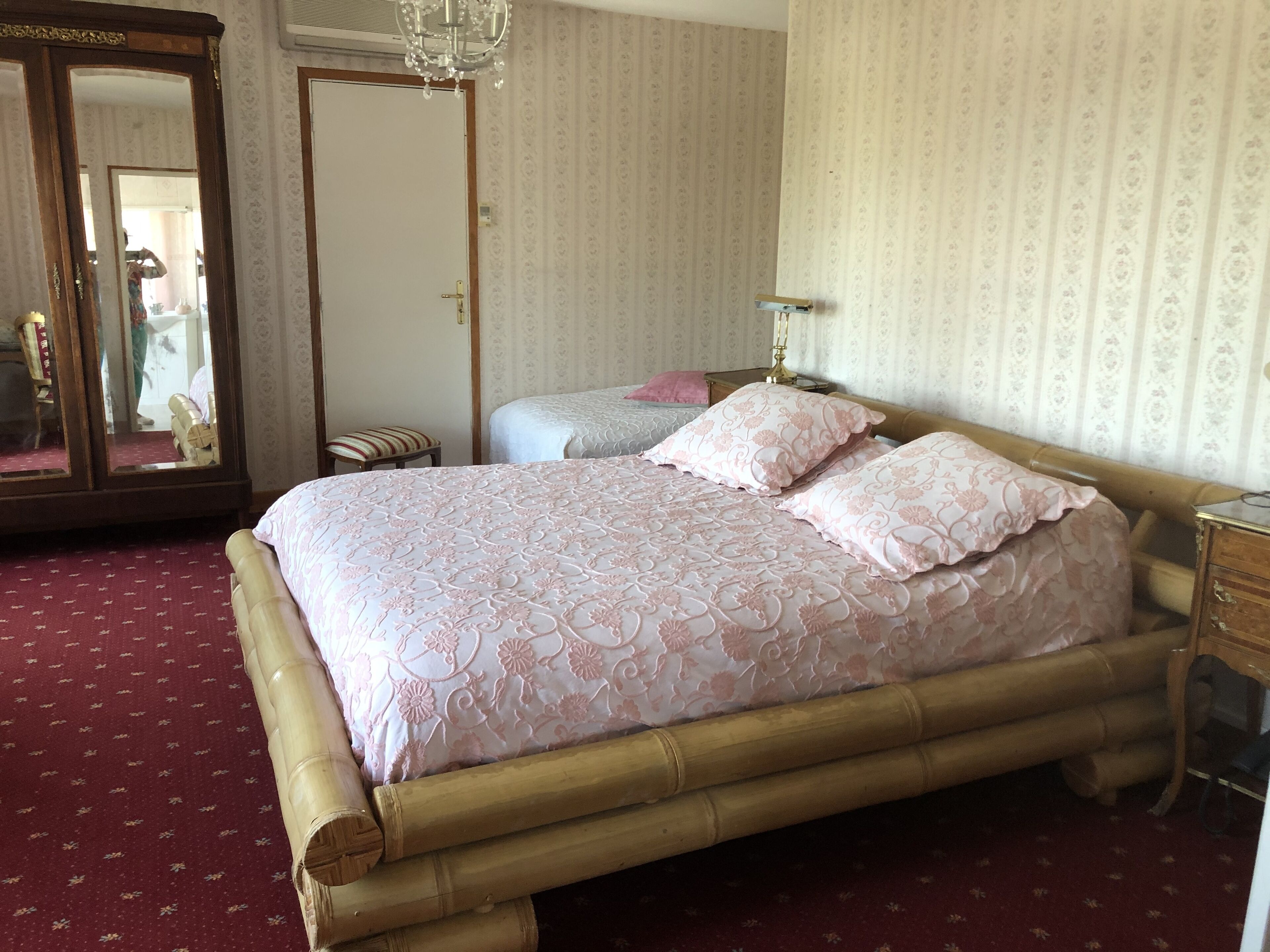 A room with a large bed, a wooden wardrobe, a mirror, and a chandelier.