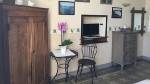 Una habitación con un armario de madera, una mesita con una orquídea en maceta, dos sillas, un televisor sobre un mueble de madera, un espejo y un aparador.