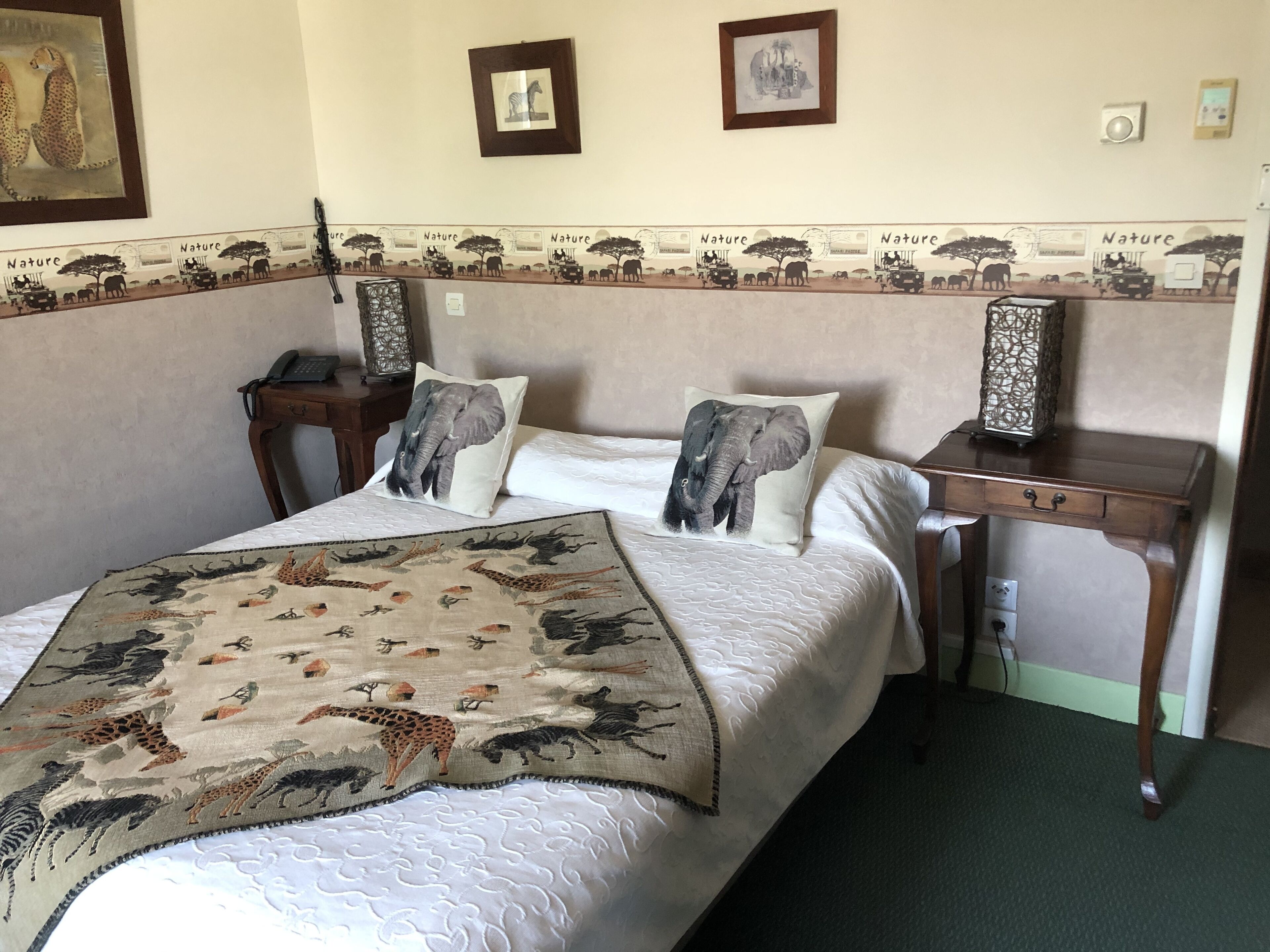 Une chambre d’hôtel comprenant un lit, deux tables de chevet, un bureau et un mur décoré sur le thème de la nature.