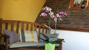 Un banco de madera con una planta verde en una maceta a rayas, una pared amarilla y una pared de ladrillo con una ventana.