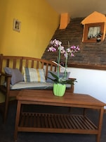 A wooden bench with a green plant in a striped pot, a yellow wall, and a brick wall with a window.