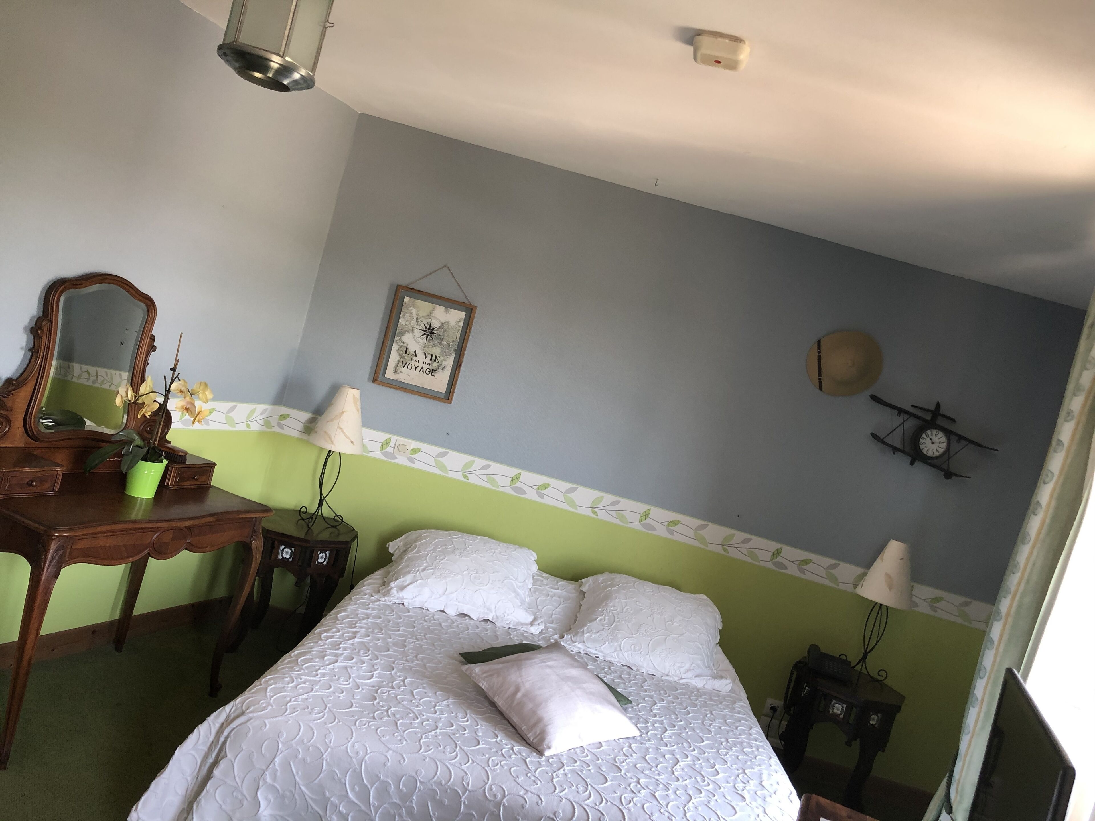 A bedroom with a bed, a dresser, a mirror, a wall clock, and a framed quote.