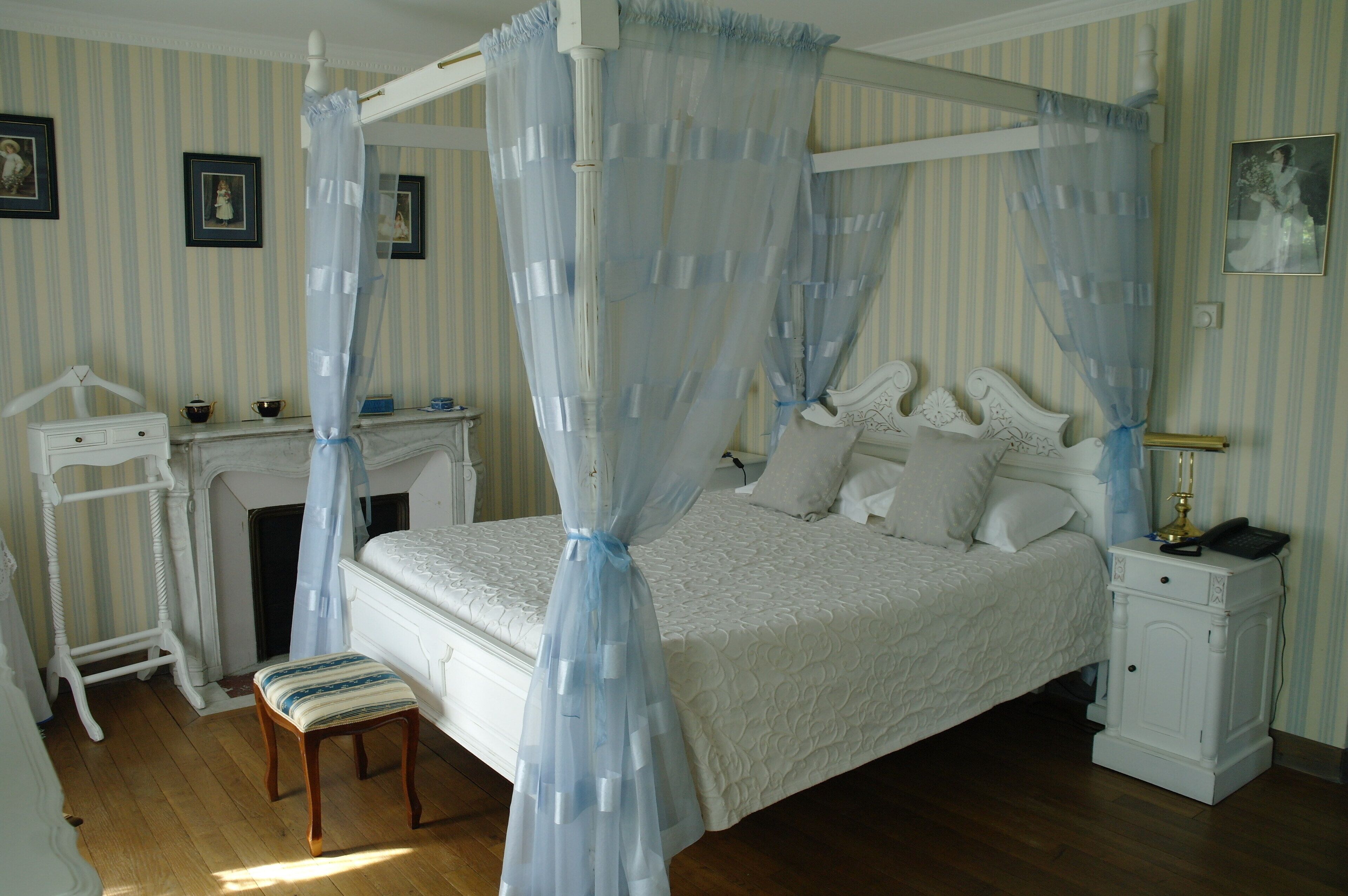 A four-poster canopy bed with a white headboard, a bedside table with a lamp, and a small cabinet.