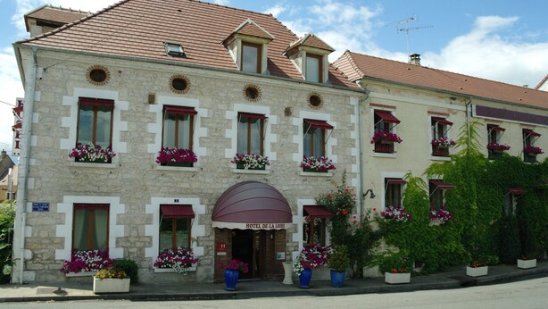 Un edificio de piedra con tejido rojo, múltiples ventanas con jardineras florales, y un letrero que dice "HOTEL DE LA LOIRE".