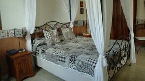 Una cama con dosel, una colcha estampada, una mesita de noche de madera con un teléfono y un armario de madera en un dormitorio.