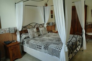 A four-poster bed with a patterned bedspread, a wooden nightstand with a telephone, and a wooden wardrobe in a bedroom.