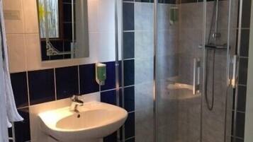 Un baño con un lavamanos blanco, cabina de ducha con mampara de vidrio y un espejo con marco decorativo.