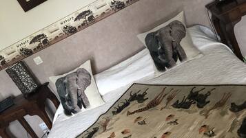 Una cama con colcha de motivos naturales que muestra animales, cabecera con escena natural y un cuadro en la pared.