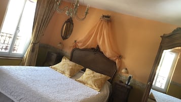 A bedroom with a large bed, a chandelier, a nightstand, a mirror, and a window with curtains.