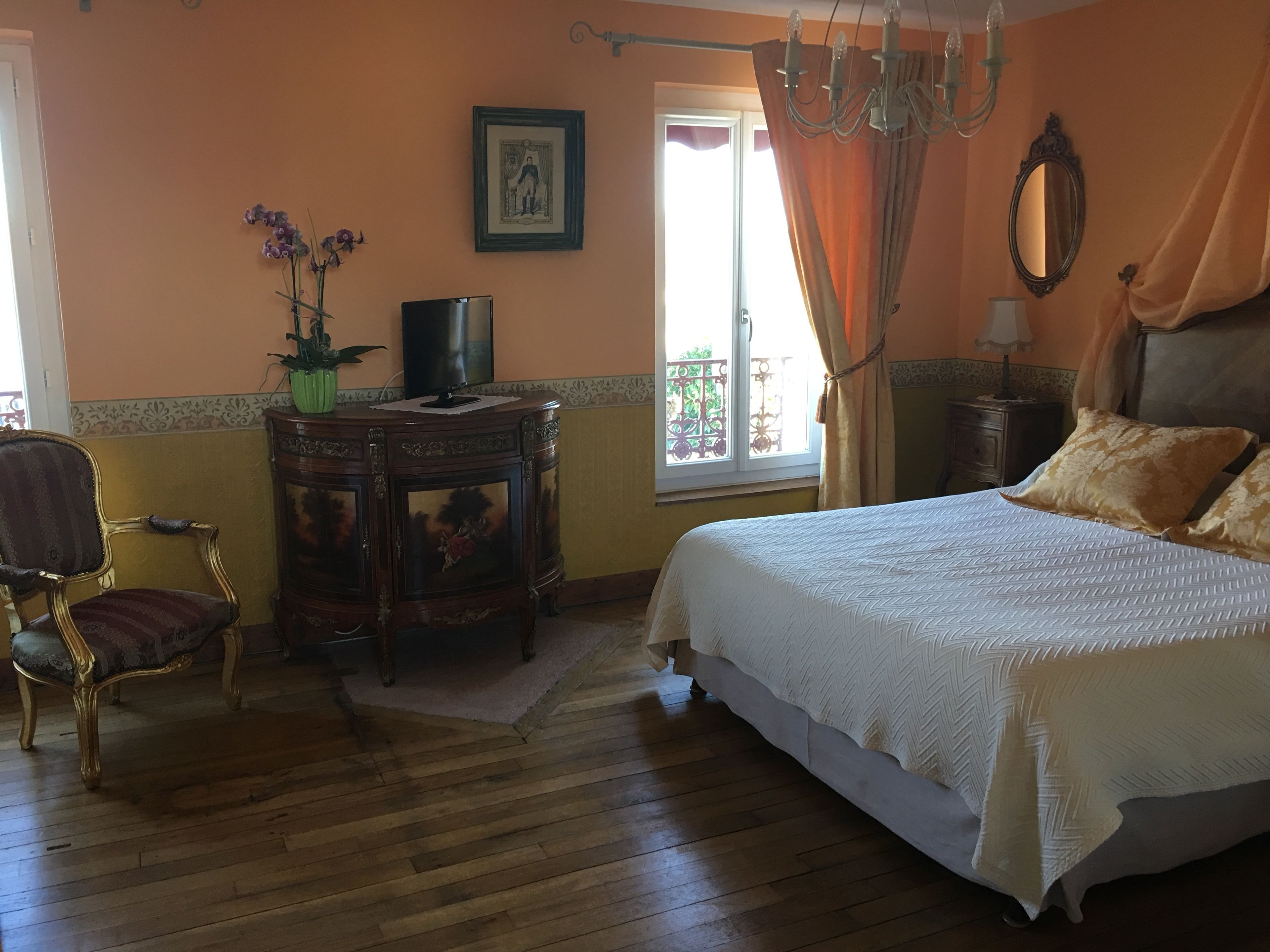 A bedroom with a large bed, a wooden nightstand, a chair, a dresser, and a television.