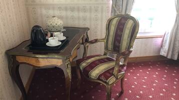 Een kamer met een fauteuil in vintage-stijl, een klein tafeltje met een theepot en kopjes, en een kamerbreed tapijt met dessin.