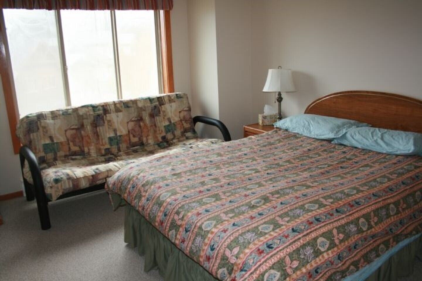 Une chambre à coucher avec un lit, une chaise, une table de chevet et une fenêtre.
