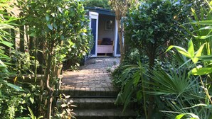 Een tuinpad dat leidt naar een klein gebouw met een open deur, omgeven door weelderige begroeiing.