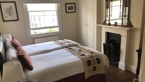 Een slaapkamer met een tweepersoonsbed, een nachtkastje met een lamp, een open haard en een raam met uitzicht op gebouwen.