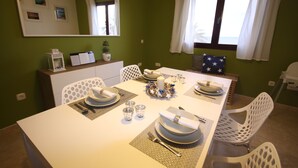 A dining area with a white table set for four, a mirror above the table, and a window with curtains. - Apartment PANORAMA Great View, WiFi, 50m beach (Costa Calma)