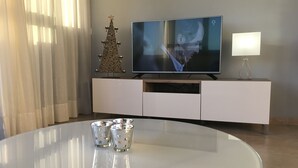 A modern living room with a flat-screen TV on a white entertainment unit, a decorative Christmas tree, and a round dining table with three glasses. - Apartment PANORAMA Great View, WiFi, 50m beach (Costa Calma)