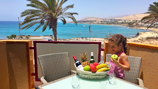 A balcony with a table, chairs, and a fruit basket. - Apartment PANORAMA Great View, WiFi, 50m beach (Costa Calma)