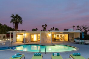 Un área junto a la piscina con sillones reclinables, una piscina y un edificio con patio abierto.