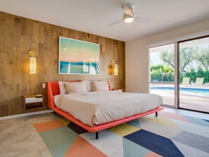 Un dormitorio con una cama grande, una pared de madera, un cuadro, dos apliques y vista a una piscina.
