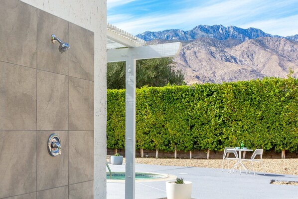 Un patio moderno al aire libre con piscina, pérgola blanca y vistas a las montañas.