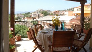 A terrace with a table set for two, overlooking a residential area with houses and hills. - Apartment in residence with panoramic sea view terrace SEA VIEW (Santa Maria Navarrese)
