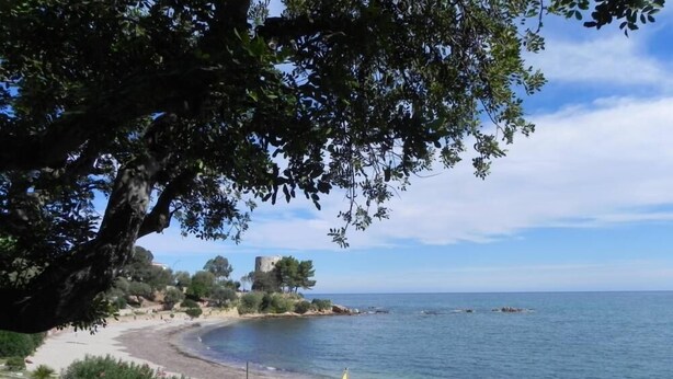 A coastal landscape with a sandy beach, a small white building, and a flagpole with a yellow flag. - Apartment in residence with panoramic sea view terrace SEA VIEW (Santa Maria Navarrese)