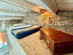 Un dormitorio de buhardilla acogedor con suelo de madera, una cama con ropa de cama a rayas, una maleta y una pared de piedra.