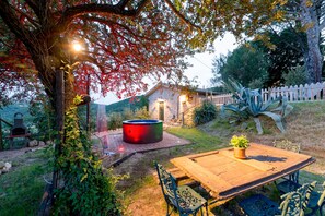 Un entorno rústico al aire libre con una mesa y sillas de madera, un jacuzzi y una parrilla de piedra.