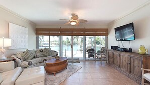 A spacious living room with a sofa, ottoman, and a television on a wooden cabinet. - 3-bedroom, 2- bath home with wide water views. (Marco Island)