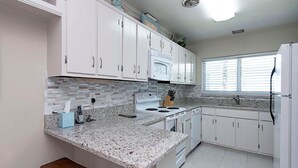 A kitchen with white cabinets, a granite countertop, a stove, and a refrigerator. - 3-bedroom, 2- bath home with wide water views. (Marco Island)
