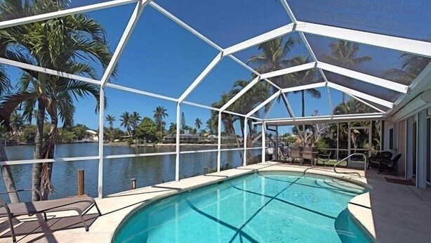 A covered swimming pool with a view of palm trees and water. - 3-bedroom, 2- bath home with wide water views. (Marco Island)