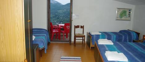 A hotel room with two beds, a wooden door, a view of mountains through a glass door, a red table and chairs, and a map on the wall.