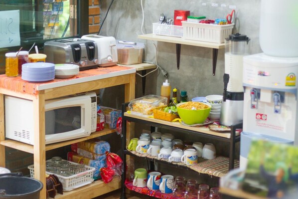 A kitchen area with various appliances and utensils, including a microwave, toaster, and shelves with mugs and containers. - DP House (Chiang Mai)