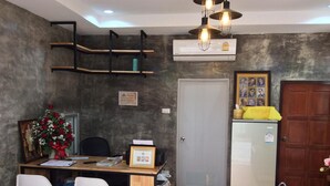 Un espacio habitable pequeño con un escritorio de madera, dos sillas, un refrigerador compacto y una puerta decorada con un collage de fotos.