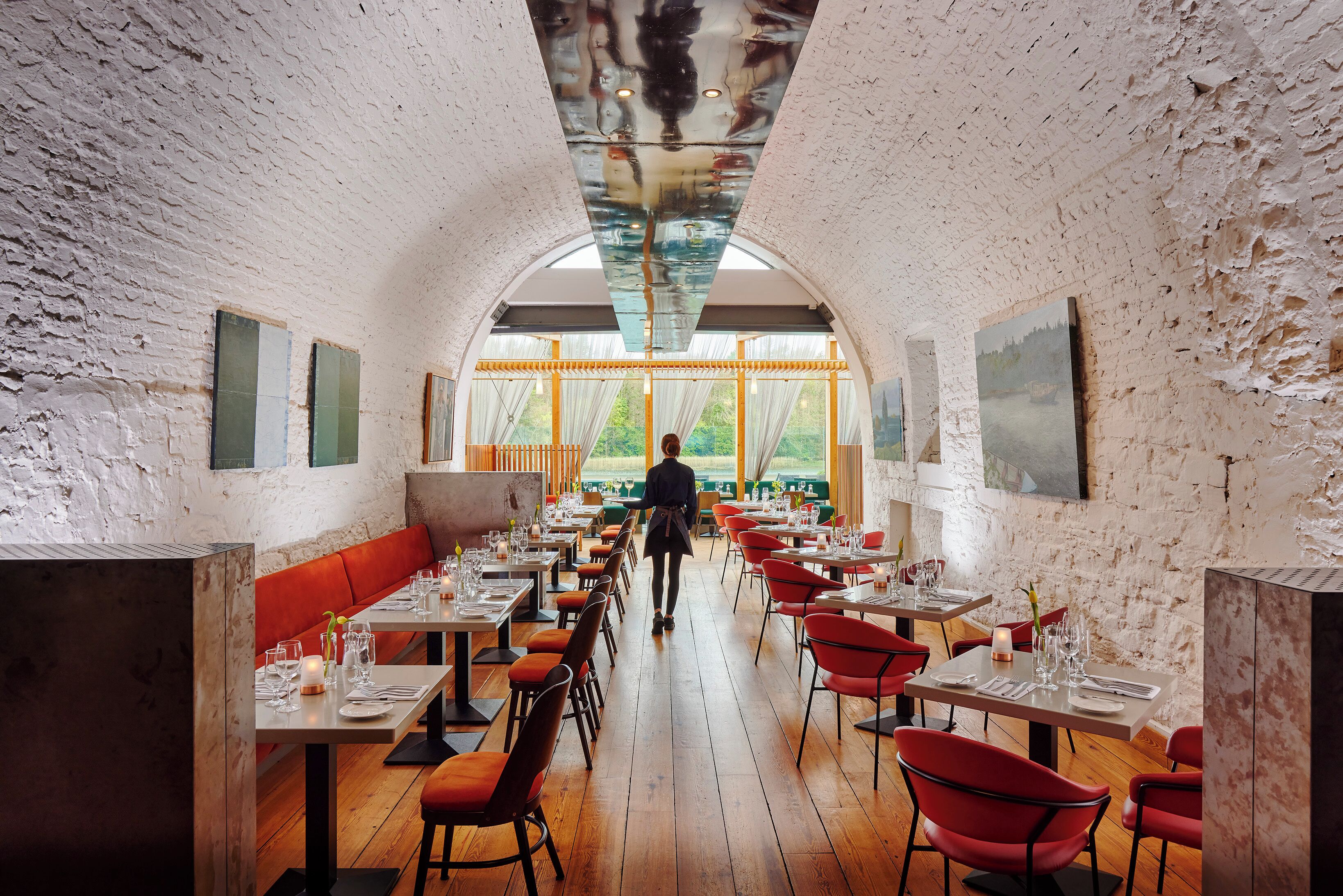 Un restaurant avec un plancher en bois, des chaises rouges et un plafond haut agrémenté d’un panneau de verre.