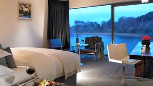 A hotel room with a large bed, a dining table with a vase of flowers, and a view of a lake. - Ice House Hotel (Ballina)