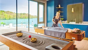 A massage room with a view of a lake, a massage table, and a relaxation area with meditation bowls. - Ice House Hotel (Ballina)