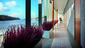 A corridor with large windows, a view of a body of water, and a row of doors. - Ice House Hotel (Ballina)